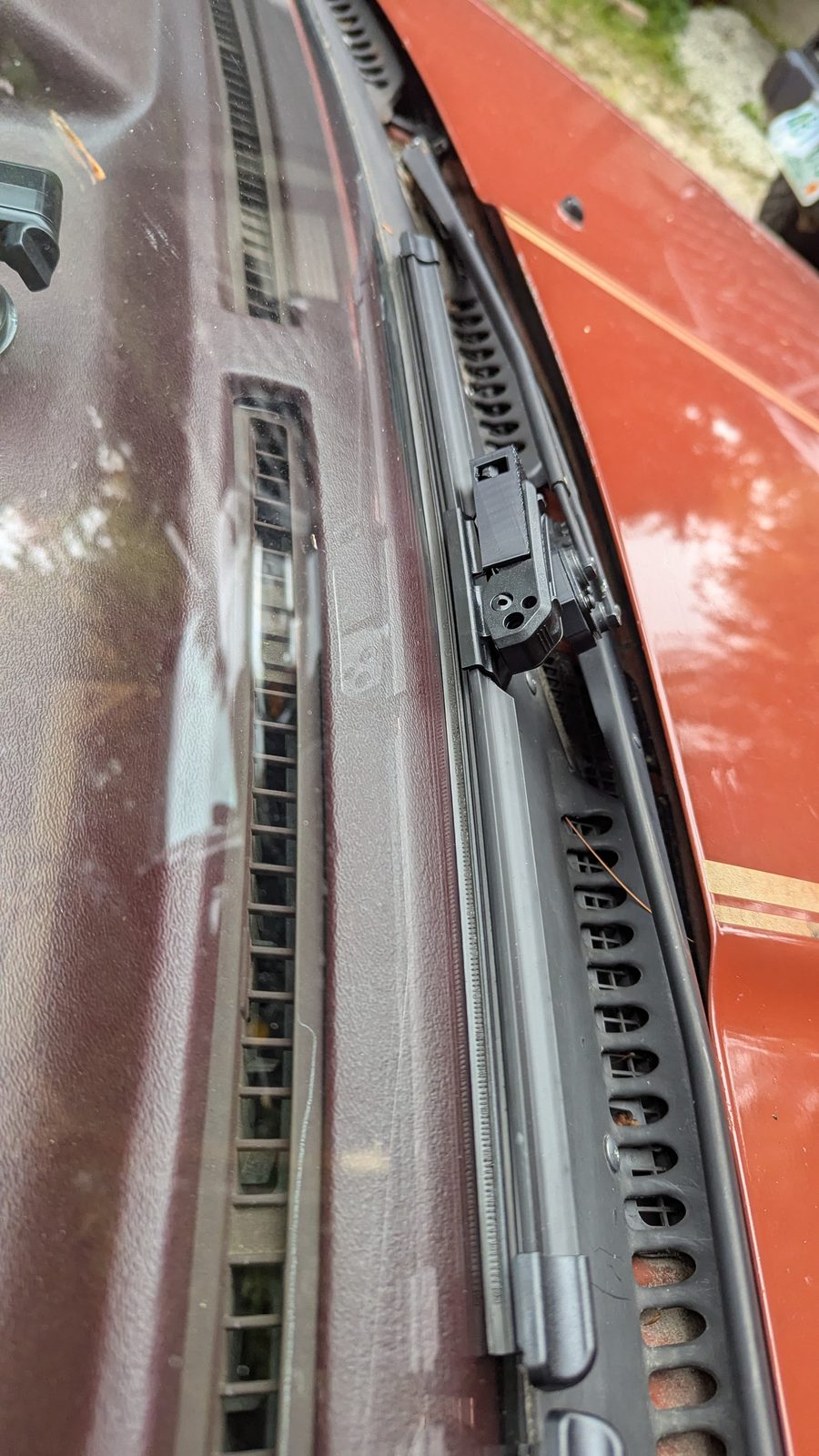 A modern blade resting along the windshield on its printed adaptor, next to the red hood.