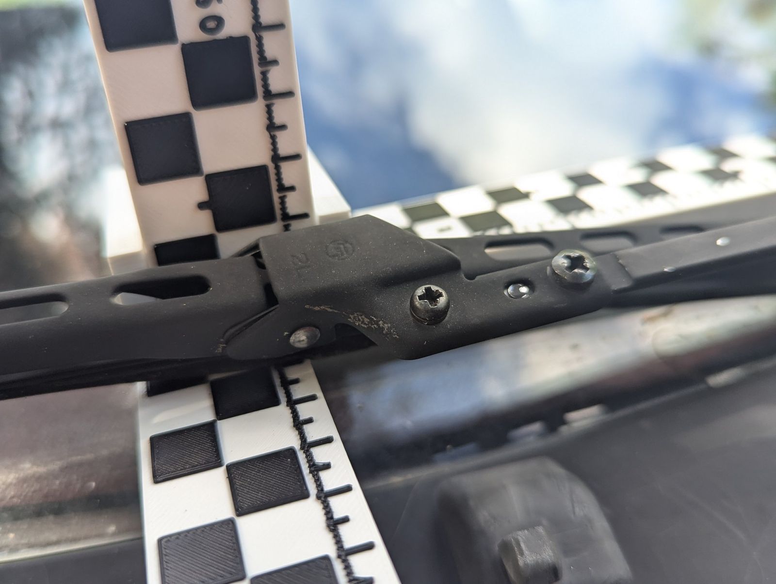 The stock passenger-side wiper carrier on the arm, next to a checkerboard scale bar.